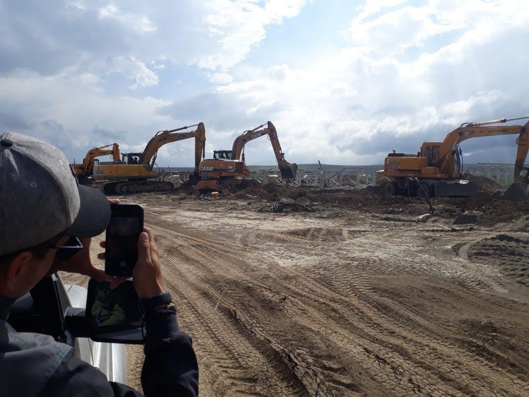 Excavators grading and clearing a utility-scale solar site in Kazakhstan under a dramatic sky