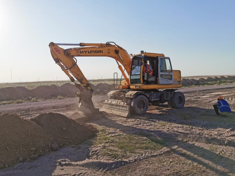 Backhoe excavator grading ground on a solar site in Kazakhstan at dusk