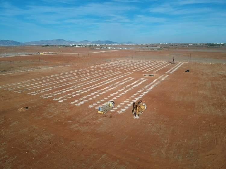 Rows of concrete pile footings laid out on a solar construction site in Cyprus, with a piling rig at work