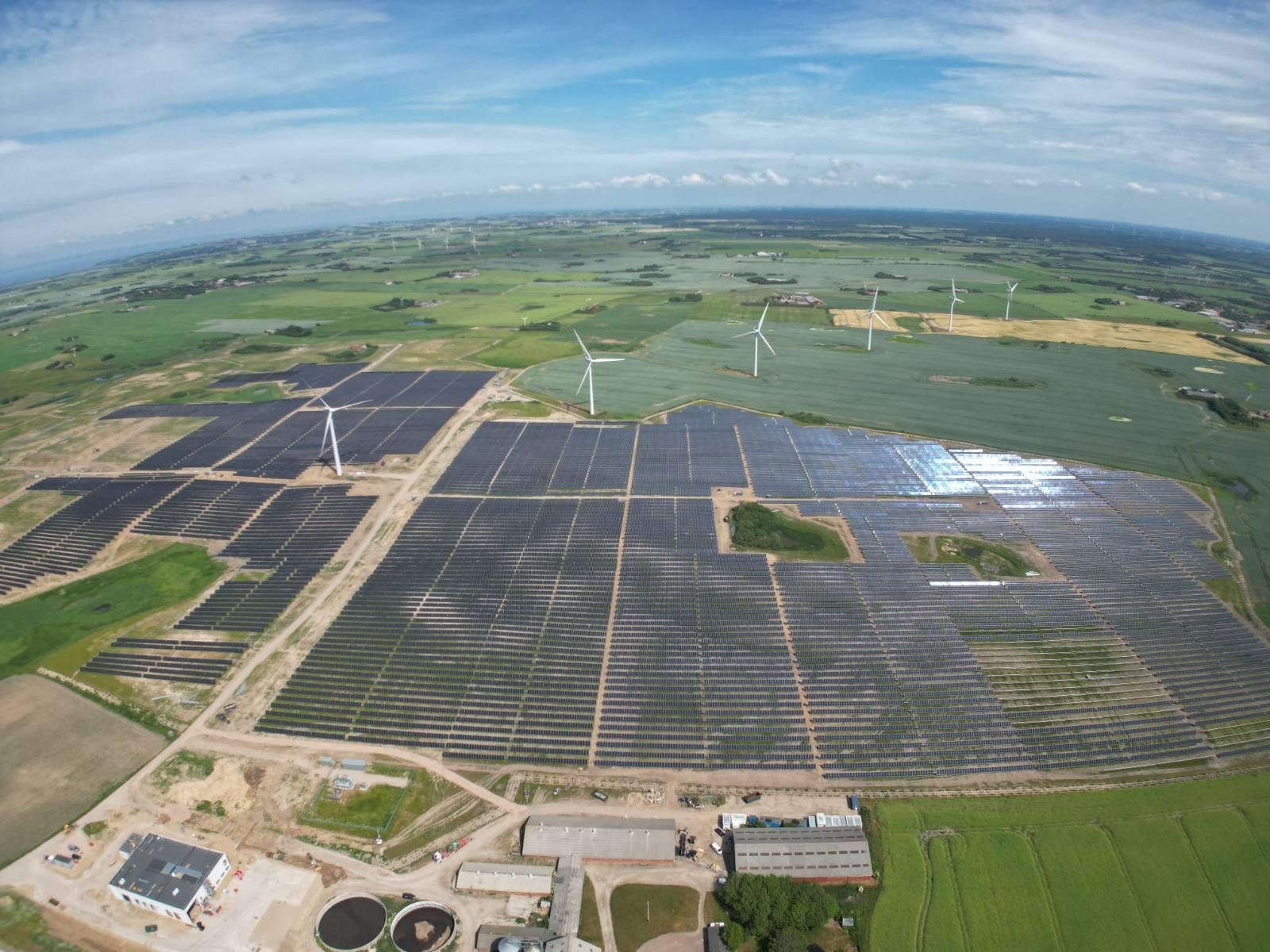Aerial view of the Skovgaard Energy hybrid solar and wind plant in Denmark, with wind turbines among rows of PV modules